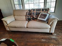 Front view of cream leather sofa with throw blanket and pillow in front of windows