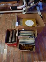 Four cardboard boxes filled with vinyl records and 78 RPM sets, viewed from above showing a variety of record sleeves and labels.