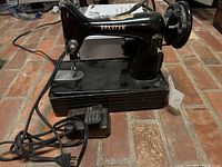 Side view of the black Spartan sewing machine showing the full machine base, foot pedal, power cord, and sewing needle area.