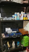 Shelving showing Mastercraft laser level in case, wooden box, assorted cans, and other tools below