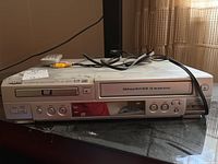 Front view of device showing DVD tray, controls, and cabling with remote control on top.
