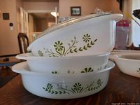 Stacked oval glass bake dishes with green floral patterns, showing side view with dish lids on top.