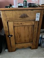 Front view of antique wood wash stand showing drawer with carved detail, single cabinet door with black metal knob, and rustic finish.