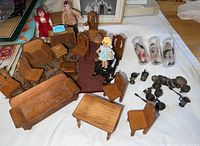 Full set of antique wooden doll furniture, three vintage porcelain dolls, and metal place settings arranged on a white cloth