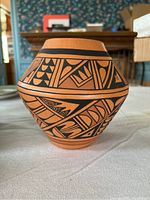 Front and side view of terracotta pottery vase with black geometric Aztec-style painting on rounded body.