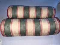 Two barrel roll pillows laid next to each other showing full length and fabric pattern of stripes in green, cream, and red with subtle dark floral jacquard details.
