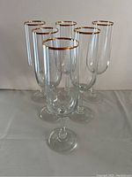 Six clear champagne flutes with gold rims arranged in a cluster showing front view
