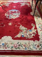 Full view of the rug showing red background with floral and dragon Sultan motifs along with border pattern and table legs on it.