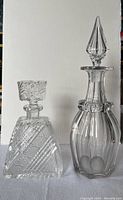 Two clear cut glass decanters side by side, one with a square stopper and the other with a pointed stopper.