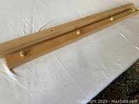 Two large light pine quilt hangers photographed horizontally on white cloth. One hanger has four large holes along its length. The other has similar holes but they are covered by smooth wooden knobs attached on top.