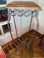 Full view of the plant stand showing the wooden top and wrought iron base with curved legs and decorative swirls.