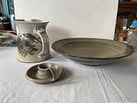 Overview photo showing three pottery items: a pitcher with painted design, a large bowl, and a candle holder.