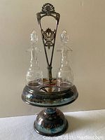 Full frontal photo of the Victorian silverplate oil and vinegar caddy with two glass bottles in place showing the front ornate handle and round base.