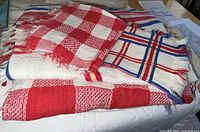 Top view of folded red and cream checkered cloth napkins on top of a larger woven plaid tablecloth with red, blue, yellow, and cream colors.