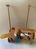 Front view of the two wooden toddler push toys showing the wooden handles and painted ends on rattle and helicopter toys.