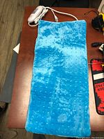 Blue flannel heating pad laid flat on wooden surface with attached control unit.