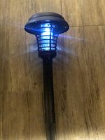 Photo of the solar bug zapper outdoor light showing black stake and protective grid with blue UV light on wooden floor.