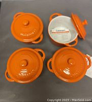 Four orange stoneware casseroles with lids arranged closed and one lid open showing interior and tag