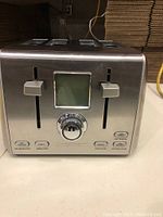 Front view showing dual control panels, two levers, LCD screen, function buttons including defrost, cancel, and bagel options.