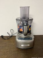 Front view of the assembled Cuisinart FP-8 food processor showing silver base, clear 8-cup bowl, control buttons, and power cord.