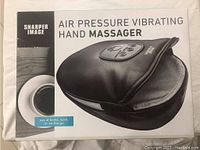 Box front showing the product name and image of the black hand massager with control panel and padded interior.