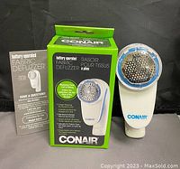 Photo of Conair fabric defuzzer with original box and user manual showing front view of device and packaging.