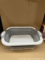 Expanded view of the collapsible basin with integrated handles and hole drains, showcasing the usable basin for washing and draining tasks. Item is fully opened showing the grey basin part within white sturdy frame.