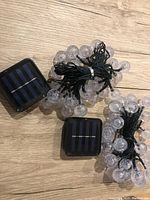 Two sets of bubble globe LED solar string lights each with a solar panel and wiring, laid out on floor showing wiring and solar panel.