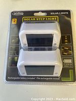 Front of packaged set showing two white solar step lights with solar panels and product branding.