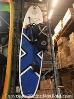 Blue and white deck of paddle board hanging vertically among other boards, showing EVA padding and bungee cords
