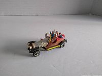 Front left angle view of the 1960s Husky Chitty Chitty Bang Bang diecast car showing silver bonnet, red seats with four figures, and yellow running boards.