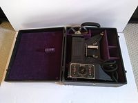 Vintage Univex 8mm film projector with its fitted carrying case open to show the projector and compartments lined in purple velvet.