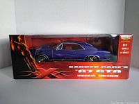 Front view of the diecast model car in original packaging showing blue 1967 Pontiac GTO with black and red themed box featuring XXX logo and character image.