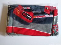 Folded Ferrari beach towel packed in clear plastic showing sponsor logos such as FedEx, TIM, Shell printed on it.