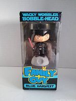 Front view of the boxed bobblehead showing Stewie Griffin dressed as Darth Vader holding a red lightsaber, with clear packaging window and blue and black box design.