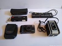 Lot of four cameras including Minolta AF Zoom 105, Kodak Twin Lens Reflex, and two other vintage cameras plus two black camera cases on white background.