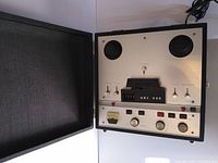 Front view of the OKI 222 stereo reel-to-reel tape recorder with case open showing two reel hubs, control knobs, and analog VU meter.
