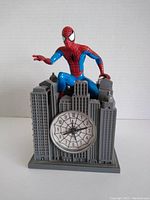 Front view of Spider-Man alarm clock with the clock face showing spider web design and Spider-Man figure on top.