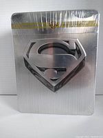 Silver metallic tin with embossed Superman logo wrapped in factory seal plastic