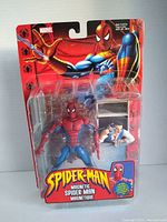 Front image of the sealed Spider-Man action figure package showing the figure and wall mount accessory inside clear plastic.