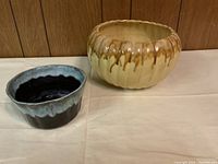Two flower pots side by side on a white cloth with wood panel background, showing size and color contrast