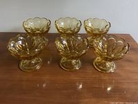 Front view of 6 amber glass dessert dishes arranged in 2 rows of 3 on a wooden surface.