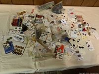 Wide array of assorted buttons on cards and plastic bags, assorted sizes and colors, plus several spools of thread, displayed on fabric surface.