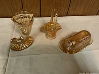 Front view of carnival glass horn vase, basket, and butter dish on cloth surface.