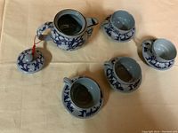 Top view of the tea set arranged on a table, showing the teapot with lid, cups, saucers, and a small bowl