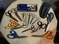 Photo showing assorted scissors of various sizes and handle colors arranged on a beige surface.