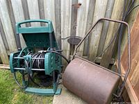 Photo of green plastic hose reel with garden hose and rusted metal lawn roller next to it
