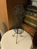 Side front view of the metal dress form showing detailed ornamental scrollwork and floral design on torso, tripod metal legs visible.