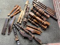 Photo showing a variety of old wooden furniture legs and parts of different shapes and finishes laid out on concrete.