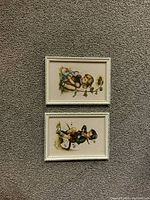 Photo showing the front sides of the two framed vintage children's illustrations with white frames on carpet.